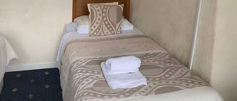 A neatly made bed with a patterned bedspread and pillows, a folded white towel on the bed, and a television mounted on the wall.