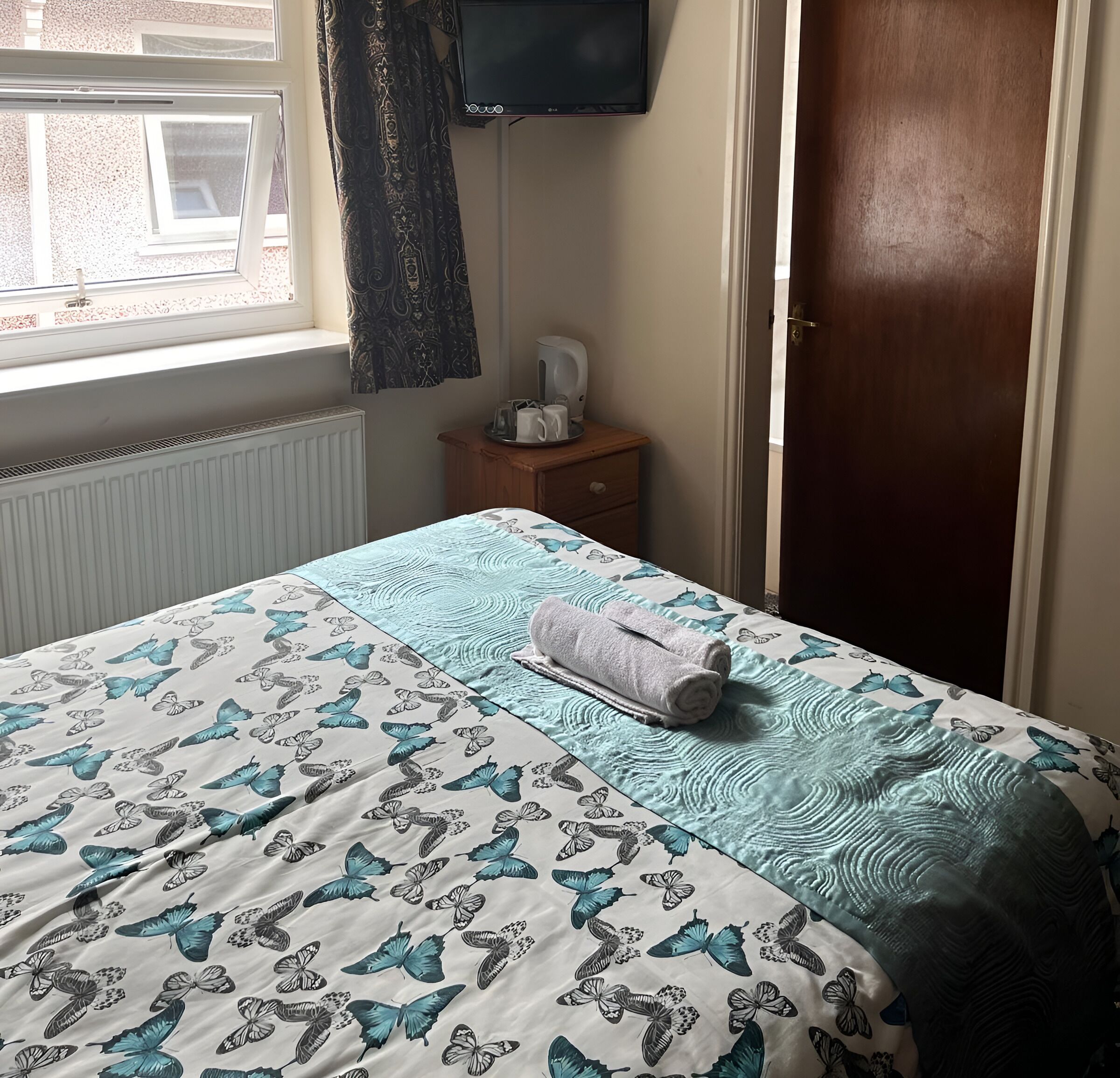 A bedroom with a bed, a nightstand, a television, and a window with curtains.
