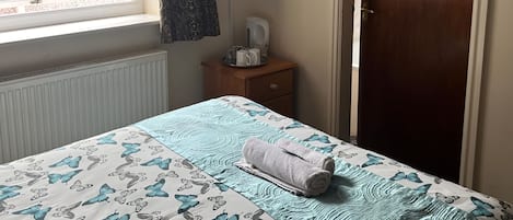 Un dormitorio con cama, mesita de noche, televisor y ventana con cortinas.