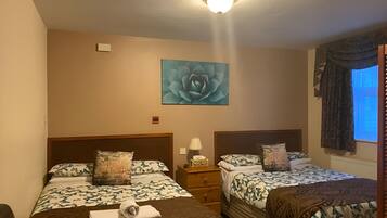 A hotel room with two beds, a nightstand, a lamp, a flower painting, and a window with curtains.