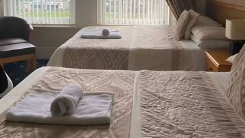 A hotel room with two beds, a chair, a nightstand, and a window with blinds.