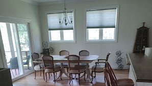 Une salle à manger spacieuse avec une grande table et six chaises, un lustre et de grandes fenêtres équipées de stores.