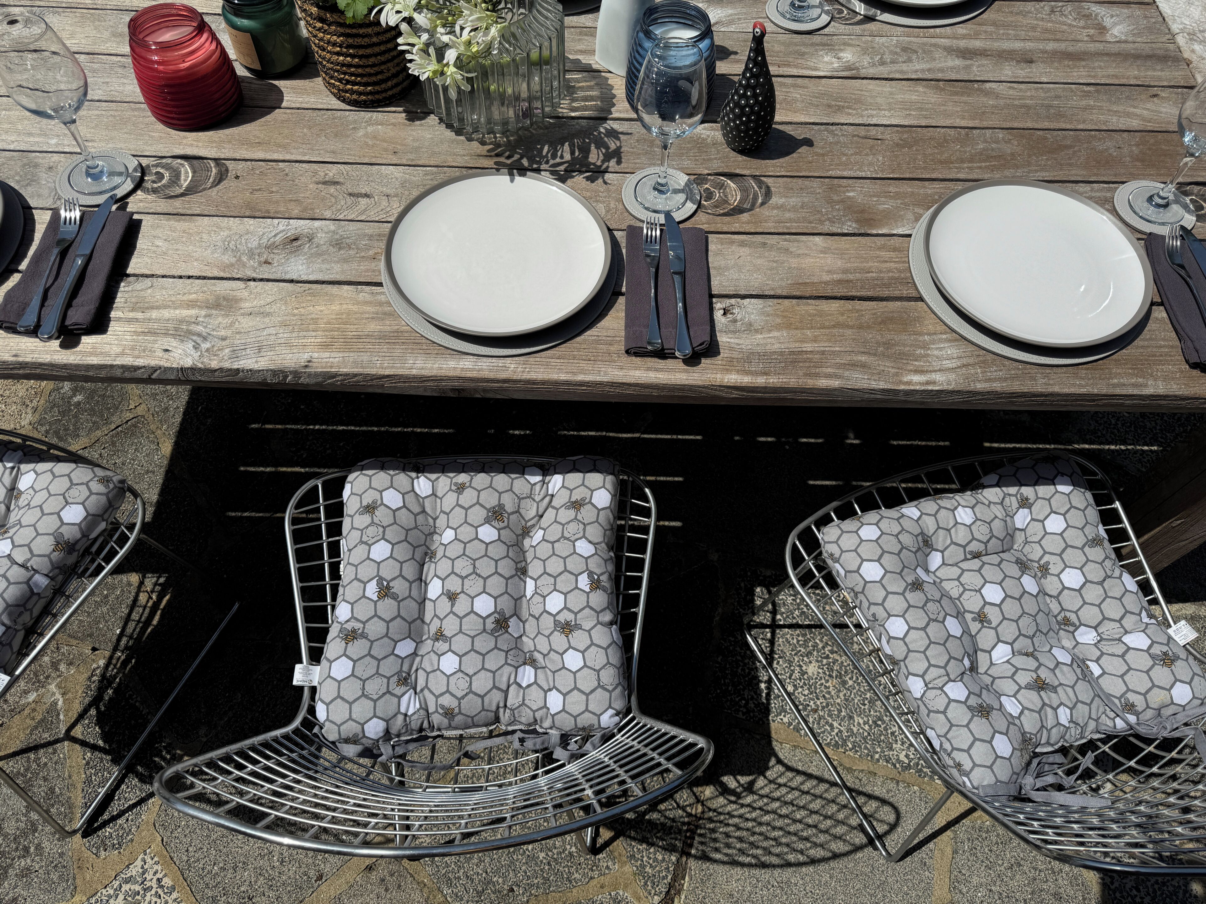 A wooden outdoor dining table with plates, cutlery, and glasses.