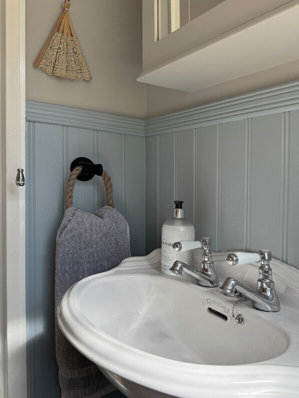 A bathroom with a white sink, two faucets, a soap dispenser, and a towel rack with a towel.