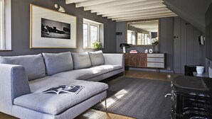 A modern living room with a grey sofa, a framed picture, a mirror, and a small wooden cabinet.