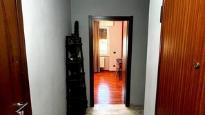 Un corridoio stretto con pavimento in legno che porta a una stanza con una finestra e una sedia.