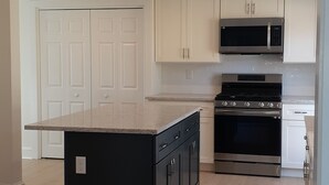 Una cocina moderna con armarios blancos, una isla central, electrodomésticos de acero inoxidable y suelo de madera.