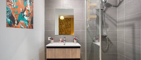 Ein modernes Badezimmer mit Duschkabine aus Glas, einem Holzwaschtisch und einem großen, abstrakten Gemälde an der Wand.