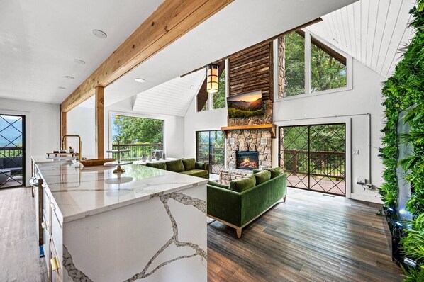 A spacious living area with a stone fireplace, a green sofa, and a large window overlooking a deck. - INACTIVE - Ritz of The Smokies (Gatlinburg)