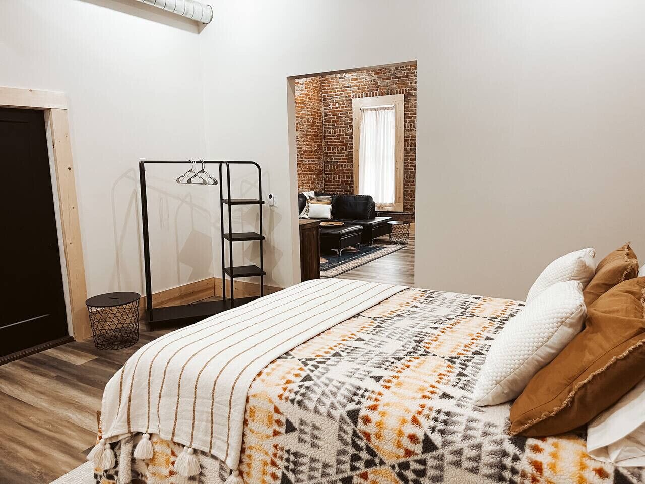 Un dormitorio con cama, perchero, una mesita redonda y pared de ladrillo.