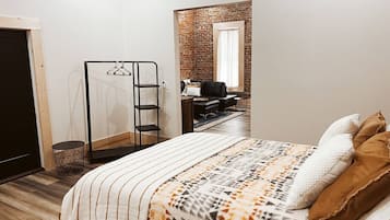 Un dormitorio con cama, perchero, una mesita redonda y pared de ladrillo.