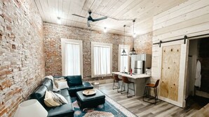 Una sala de estar acogedora con pared de ladrillo, un sofá de cuero negro, una mesa de centro y un comedor con barra.