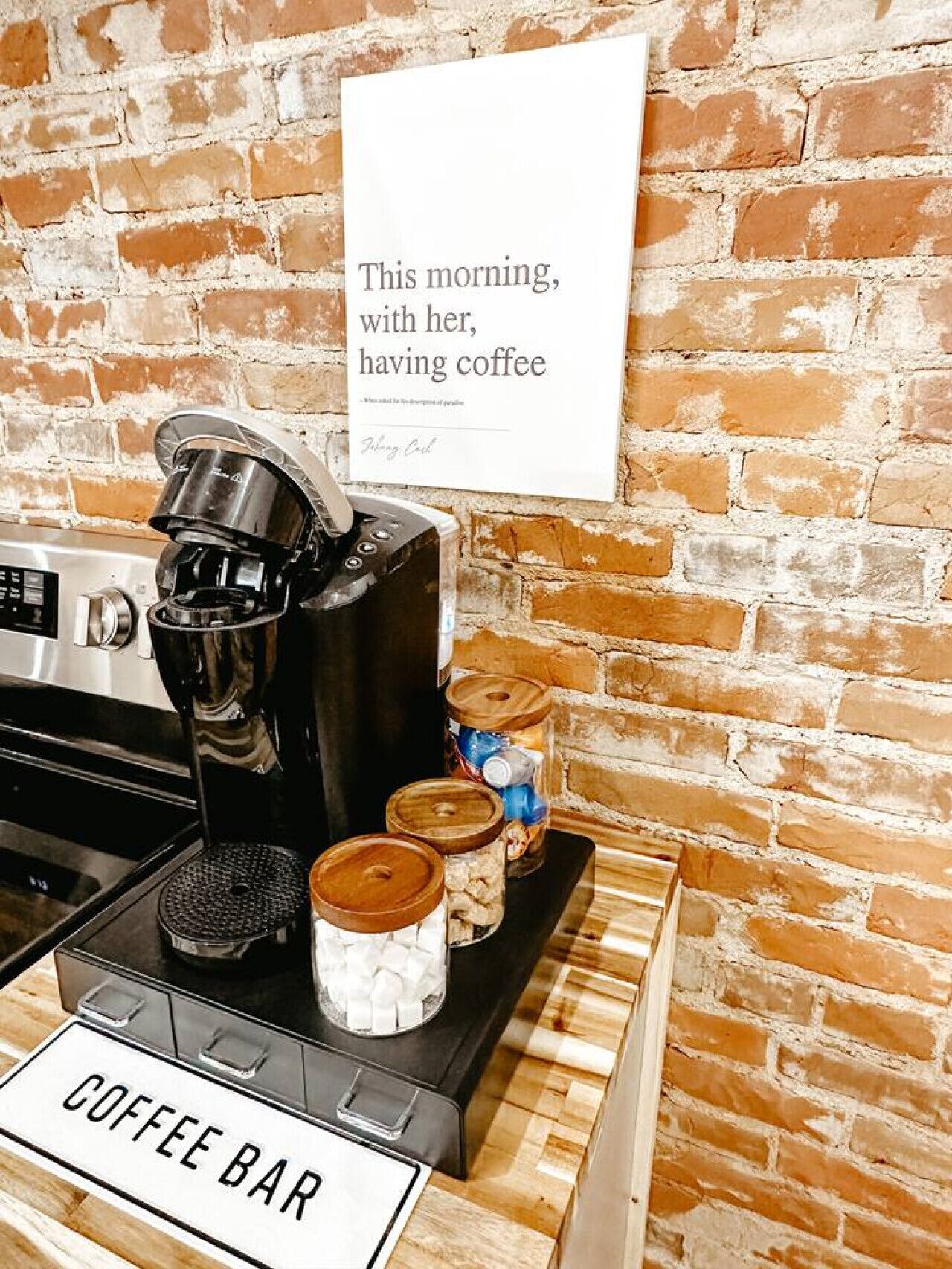 Een koffiebar met een koffieapparaat, potten koffie, en een bordje met de tekst 'Deze ochtend, met haar, koffie drinken'.