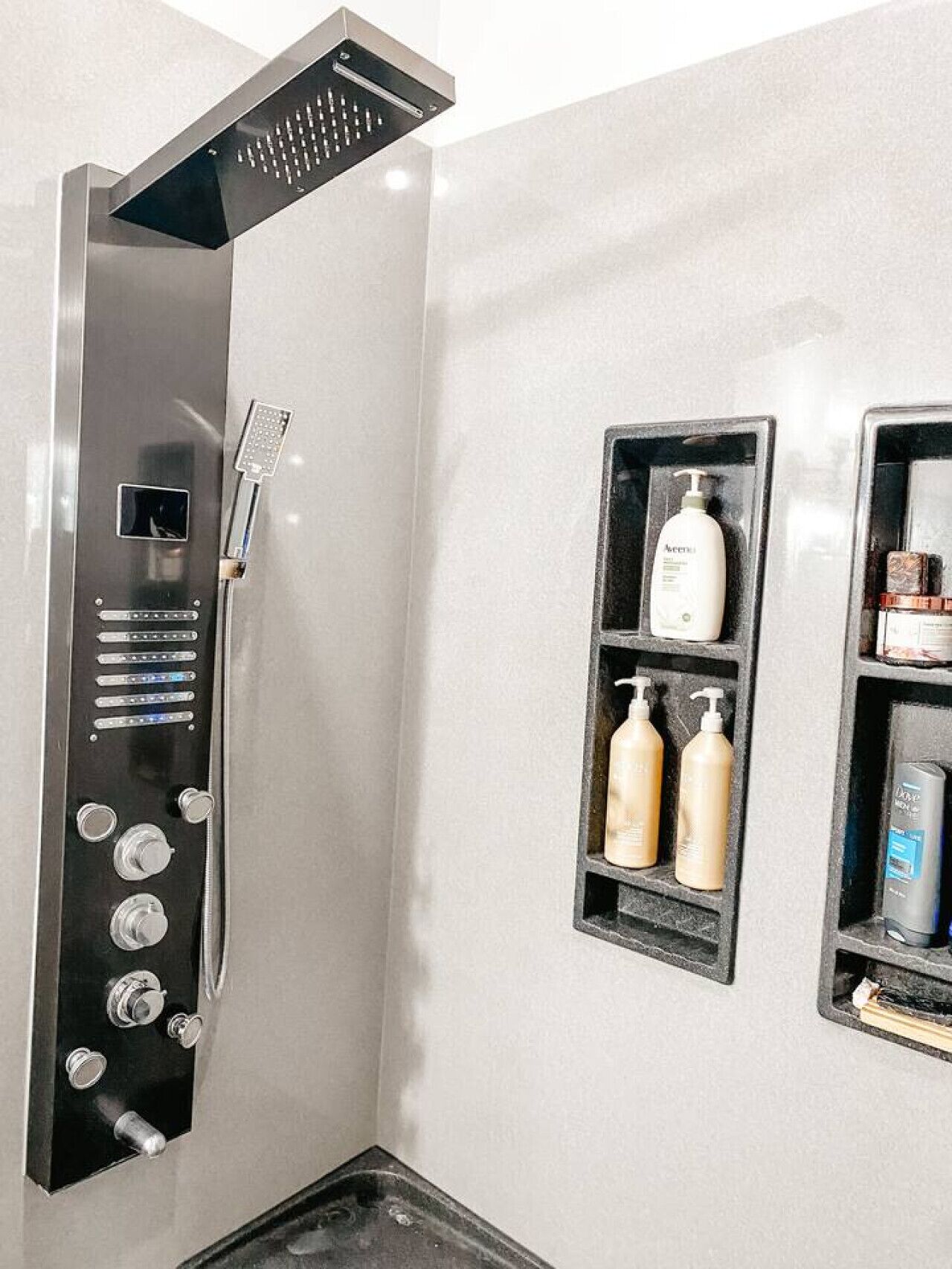Un baño moderno con ducha, panel de control y repisas con artículos de aseo.