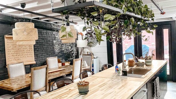 Una cucina moderna con un lungo bancone in legno, piante sospese e un muro in mattoni.
