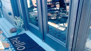 Un terrazzo in legno con un tappetino con la scritta 'hello', piante in vaso e una porta vetrata che dà su una zona salotto all'aperto.