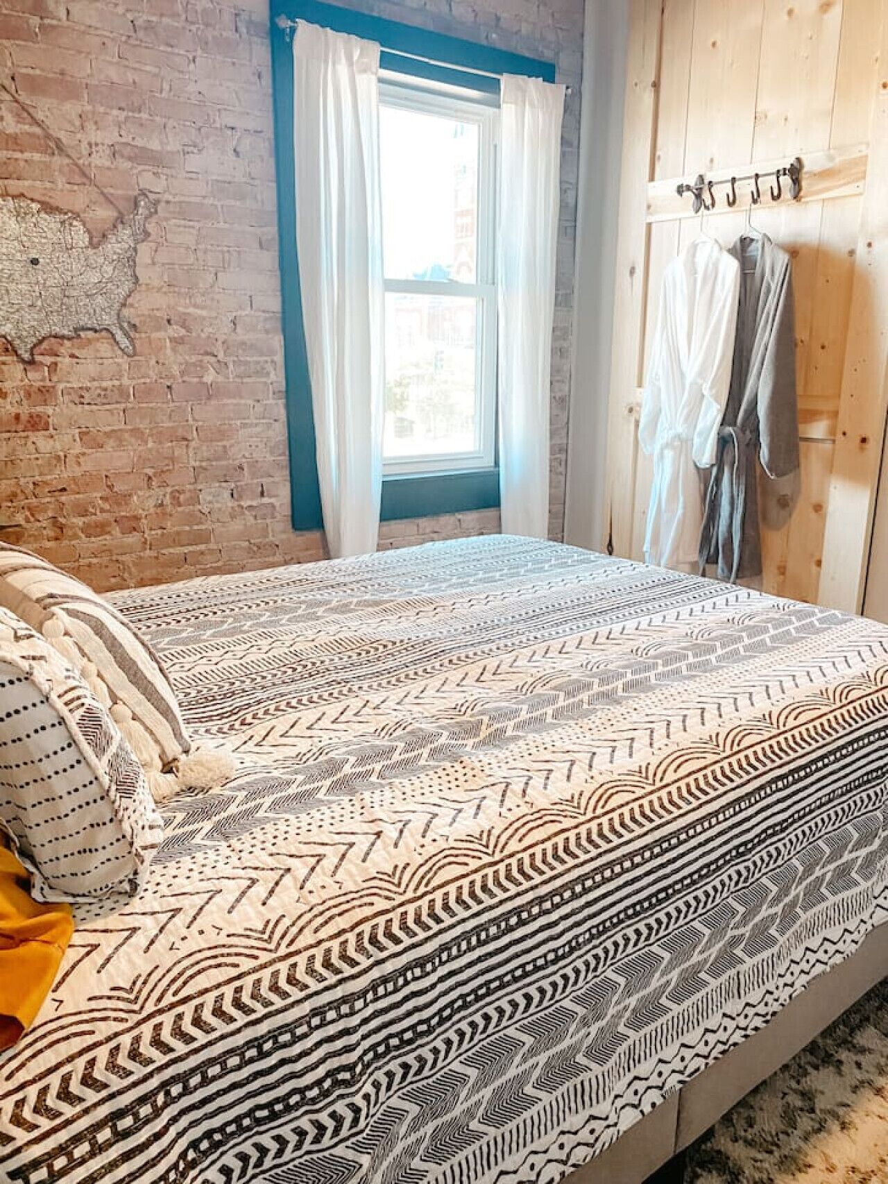 Une chambre à coucher avec une couvre-lit à motifs, une fenêtre avec des rideaux et un mur en bois orné d’une carte.
