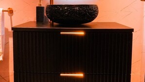 A modern bathroom vanity with a round mirror, a black sink, and a towel rack. - MY SECRET (Torrox-Costa)