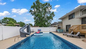 A swimming pool with a slide, lounge chairs, and a wooden deck.