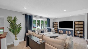 A modern living room with a sectional sofa, a flat-screen TV, and a built-in bookshelf. - Urbandale Oasis (Urbandale)