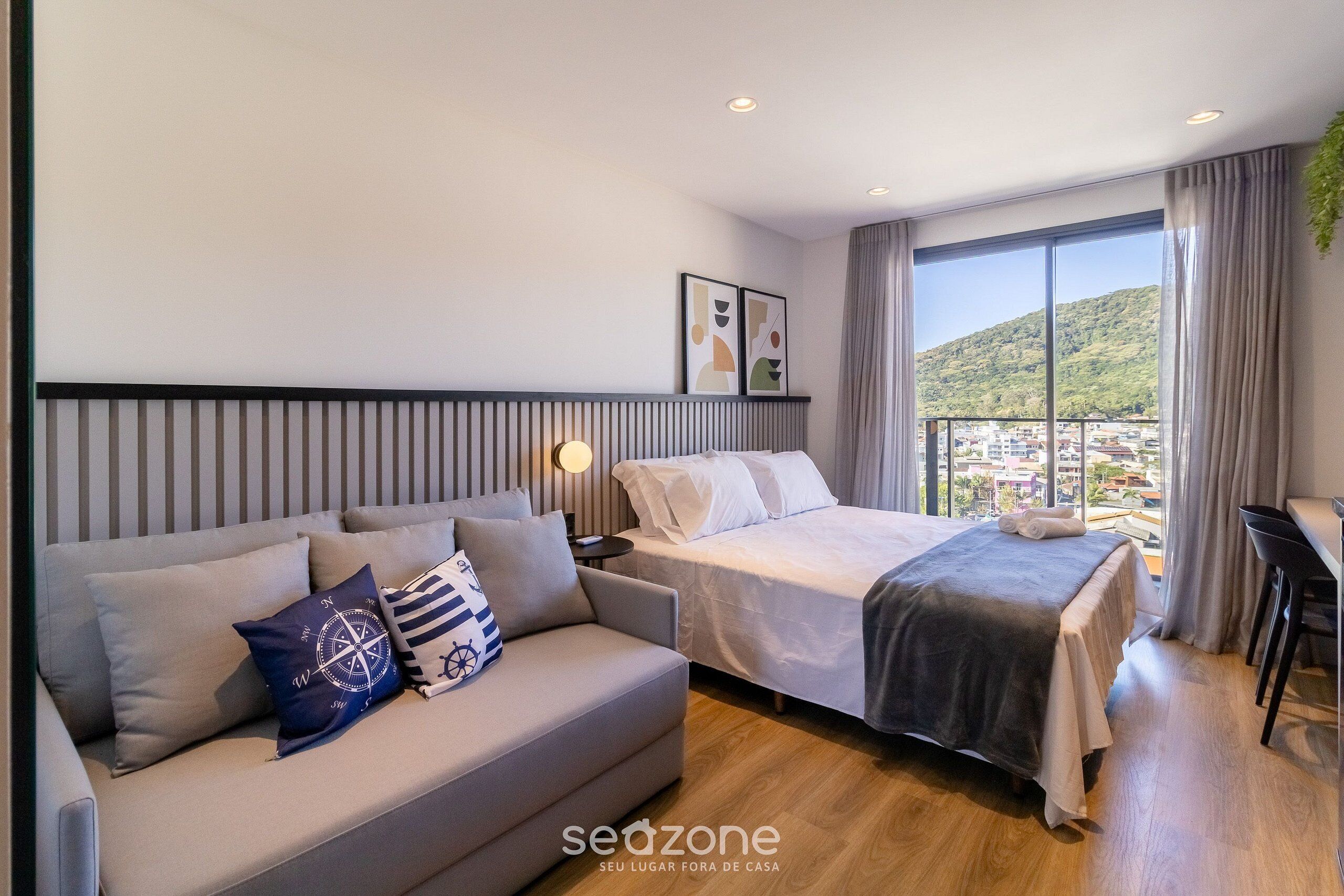 Habitación de hotel moderna con cama, sofá y un amplio ventanal con vistas a la ciudad.