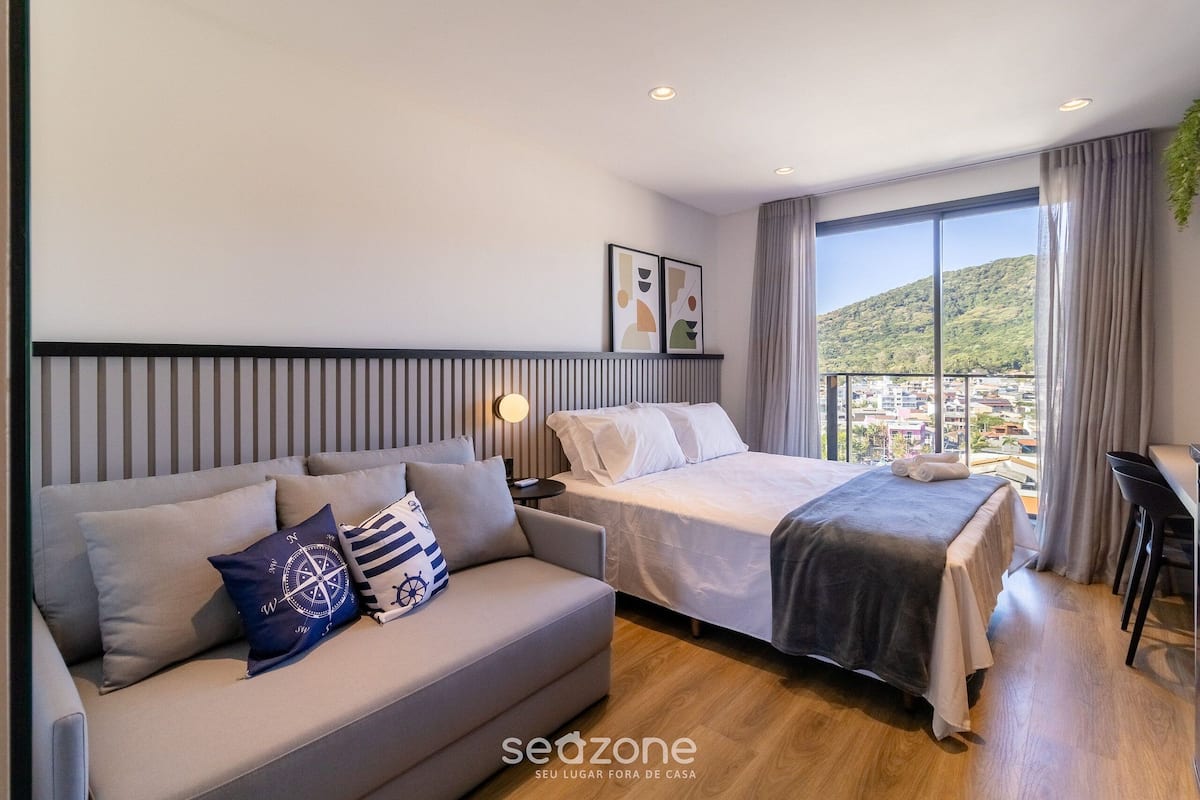 Habitación de hotel moderna con cama, sofá y un amplio ventanal con vistas a la ciudad.