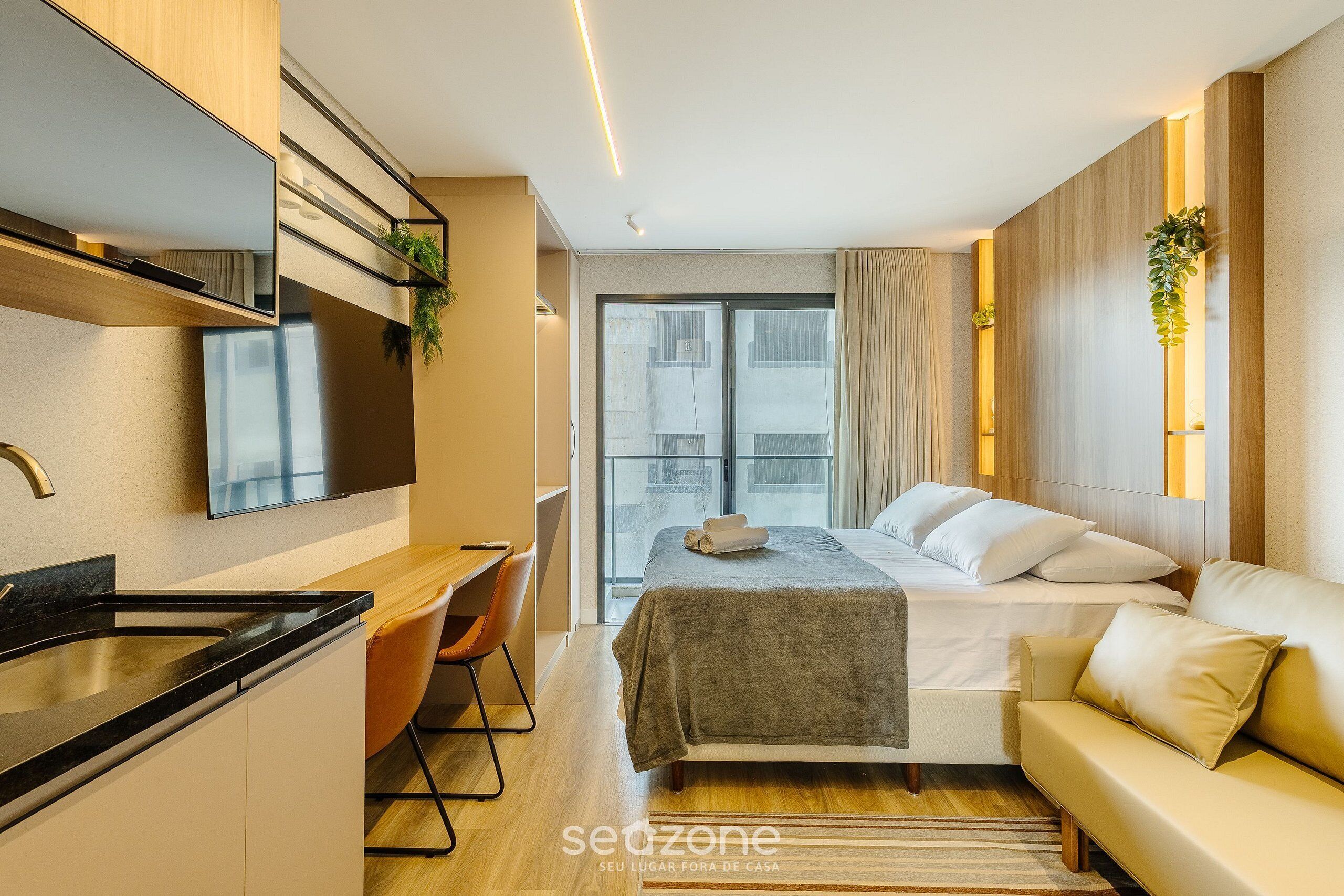 Una habitación de hotel moderna con cama, sofá, escritorio y una zona de cocina.