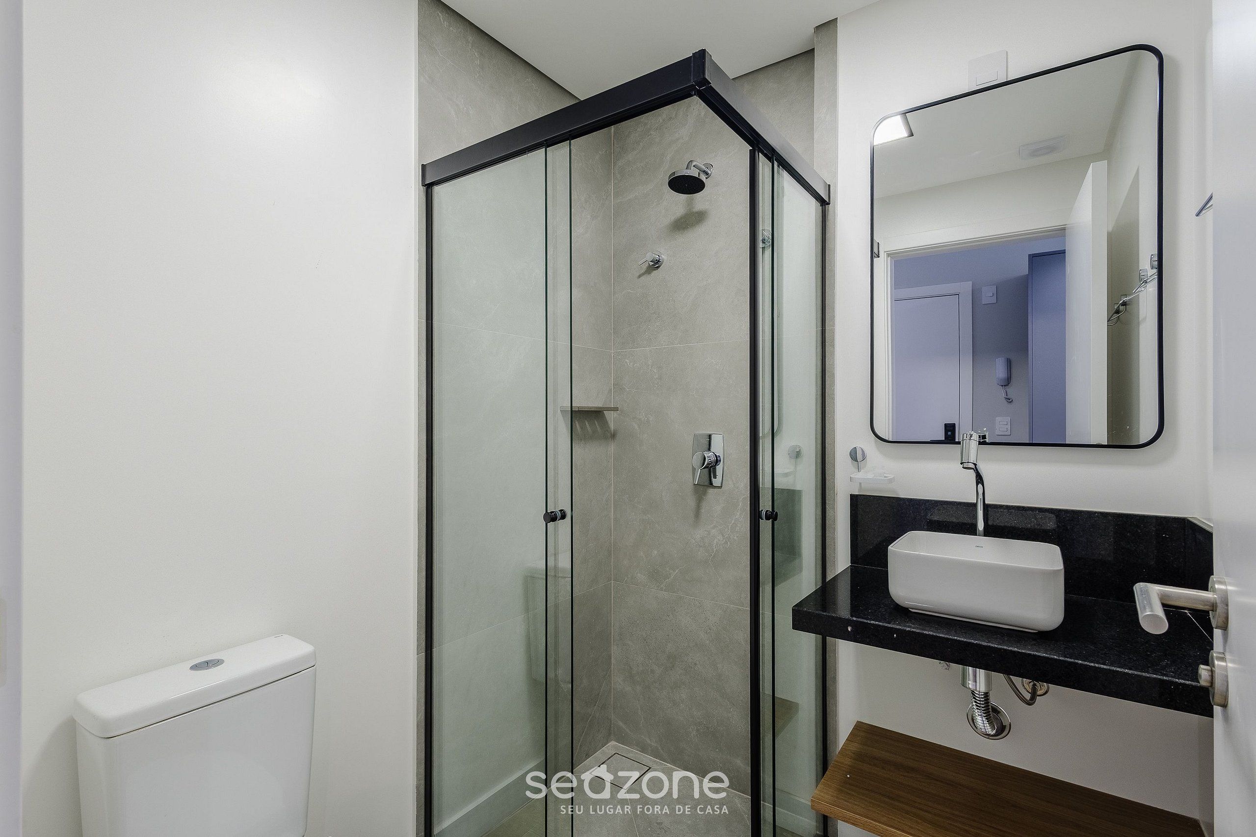 A modern bathroom with a glass-enclosed shower, a white sink, and a black countertop.
