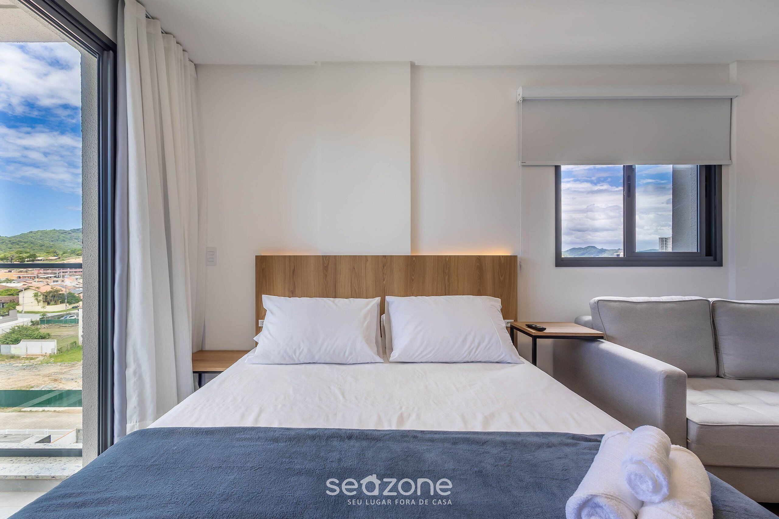 Habitación de hotel con cama, sofá, mesita de noche y vistas a la ciudad.