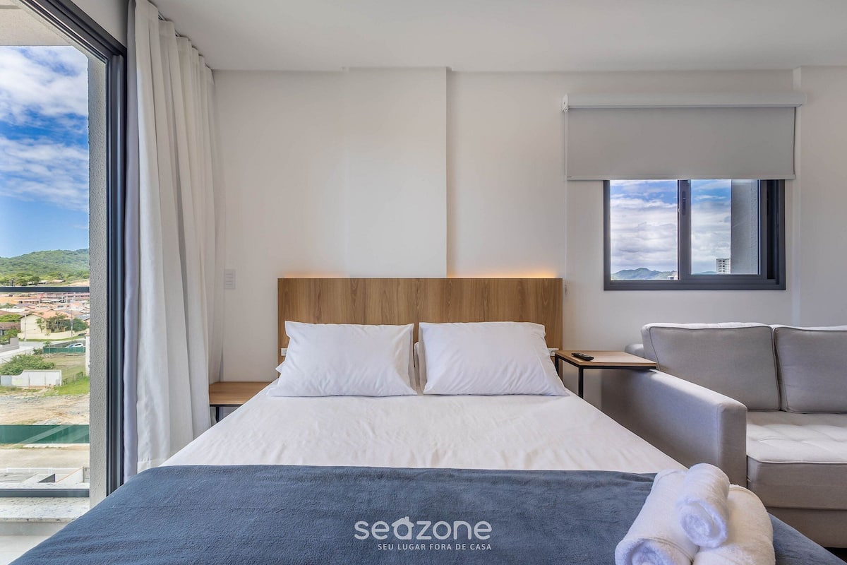 Habitación de hotel con cama, sofá, mesita de noche y vistas a la ciudad.