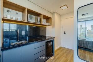 A modern kitchen with a built-in microwave, oven, and dishwasher, wooden shelves, and a large window offering a city view. - Studios With Side Sea View at Penha Spot PSO - L (Penha)