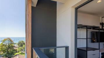 A modern balcony with a glass railing, a view of the sea, and a minimalist interior with a built-in TV shelf.