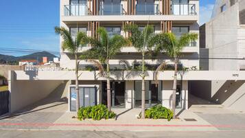 A modern building with a flat roof, multiple balconies, and a gated entrance.