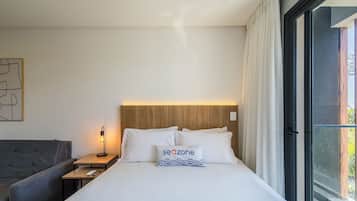 Una habitación de hotel con una cama, una mesita de noche con lámpara, un sofá y una ventana con cortinas.