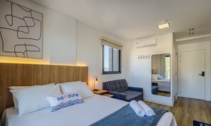 Una habitación de hotel moderna con una cama grande, una zona de estar, una ventana y un espejo.