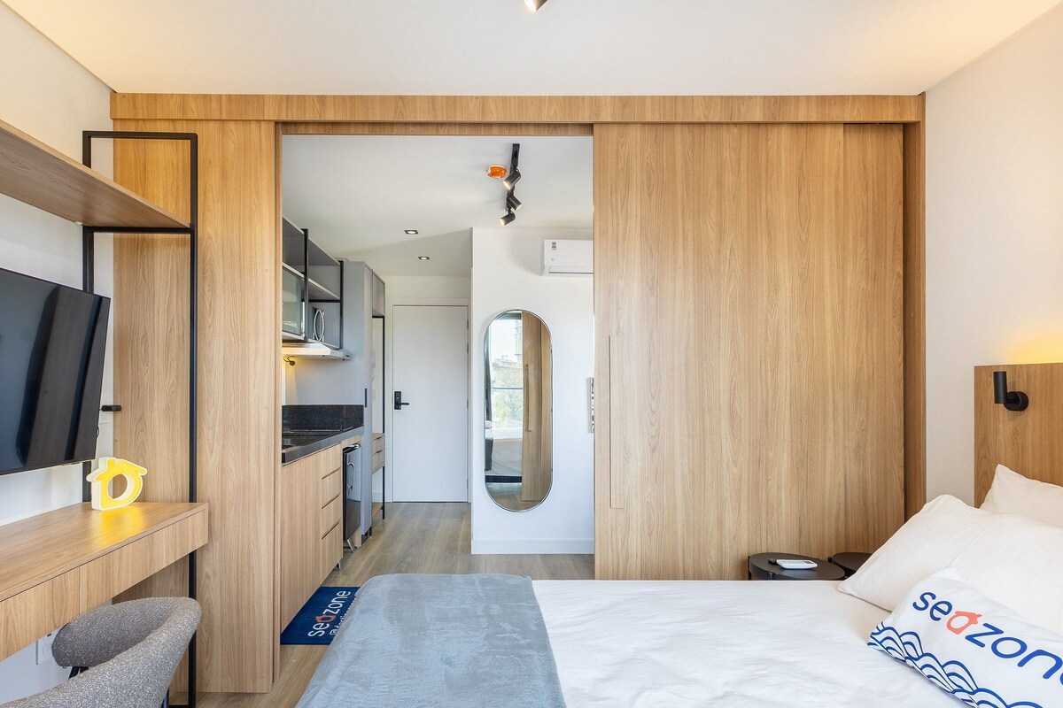 A modern hotel room with a bed, a desk, a TV, and a bathroom visible through an open door.