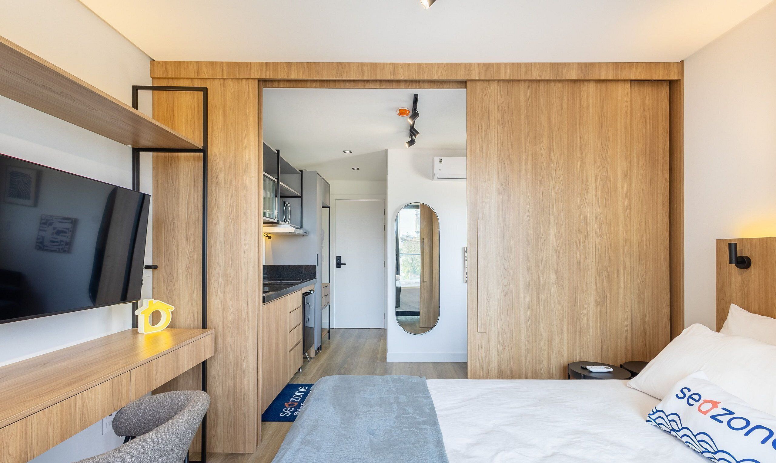 Habitación de hotel moderna con cama, escritorio, televisor y baño visible a través de una puerta abierta.