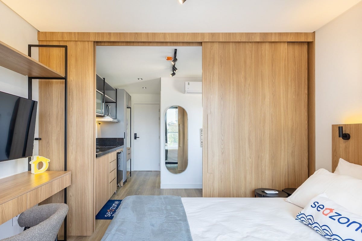 Habitación de hotel moderna con cama, escritorio, televisor y baño visible a través de una puerta abierta.