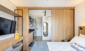 A modern hotel room with a bed, a desk, a TV, and a bathroom visible through an open door. - Studios With Side Sea View at Penha Spot PSO - L (Penha)