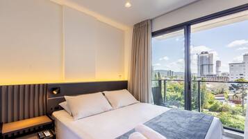 A hotel room with a bed, bedside table, and a view of the city.