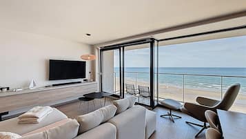 Un salon moderne doté d’un grand téléviseur, de sièges confortables et offrant une vue sur la plage.