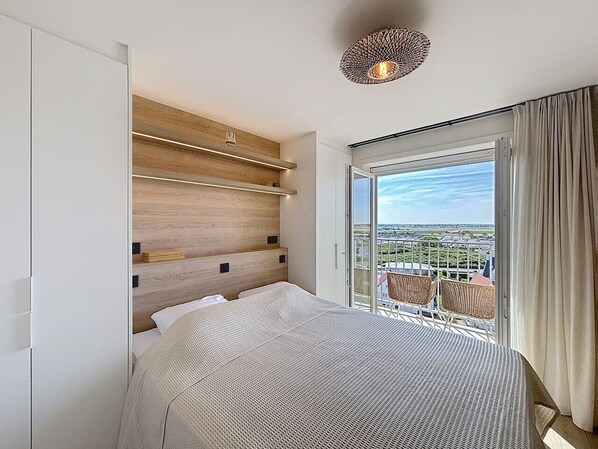 A hotel room with a large bed, a wooden headboard, a balcony with a view, and a ceiling light fixture.