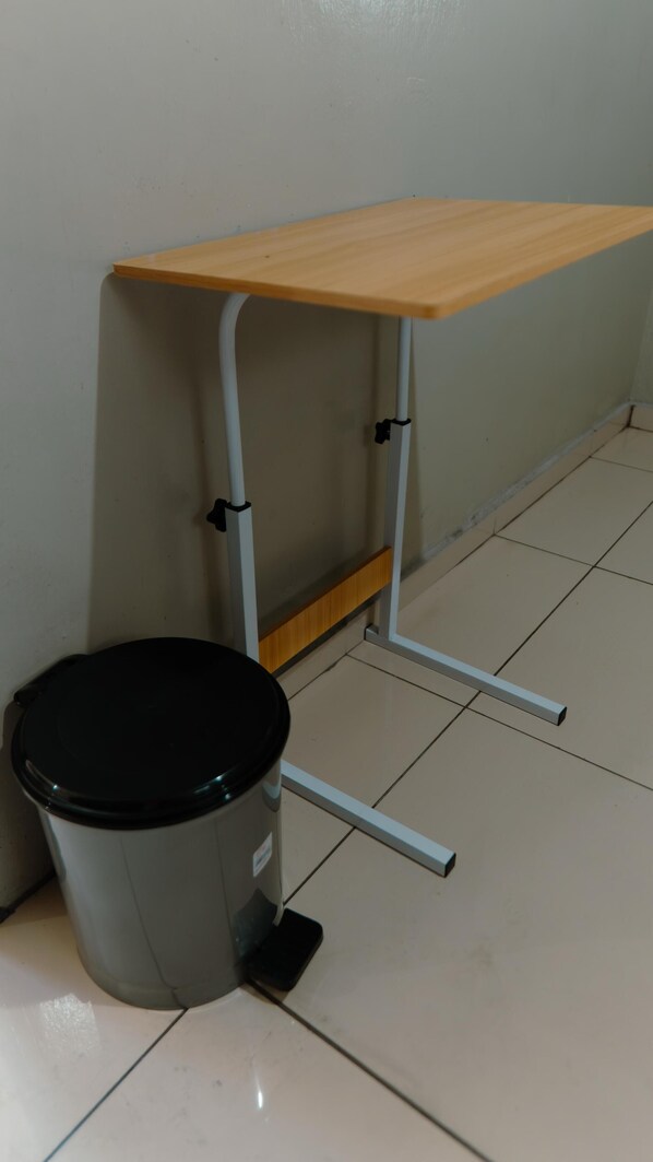 A small, portable table with a wooden top and metal legs, positioned next to a trash bin on a tiled floor.