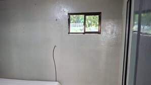 A room with a bed, a small window, a trash bin, and a door. - All inclusive apartment (San Salvador)