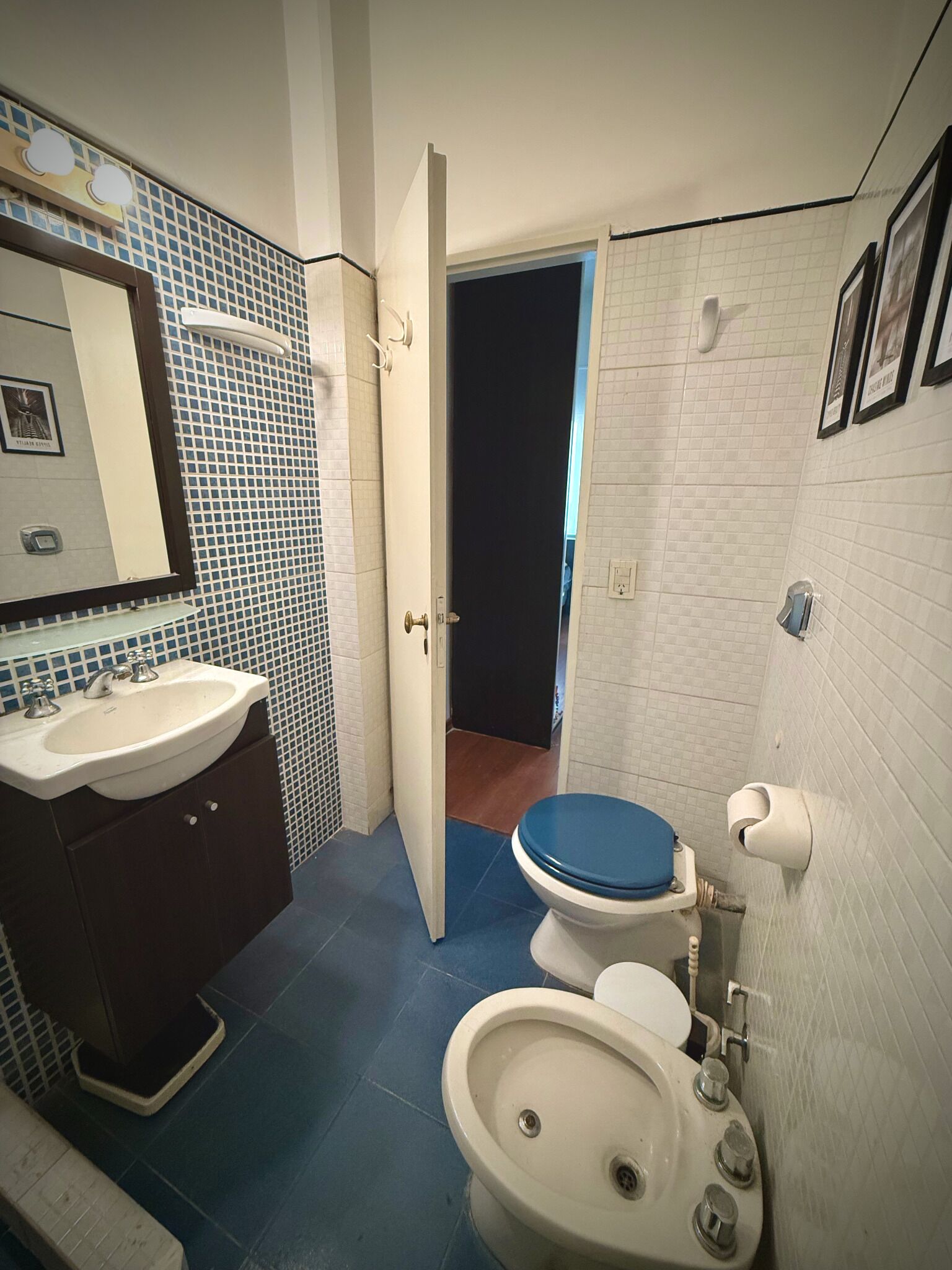 A bathroom with a sink, toilet, and bidet. There is a mirror above the sink and a door leading to another room.