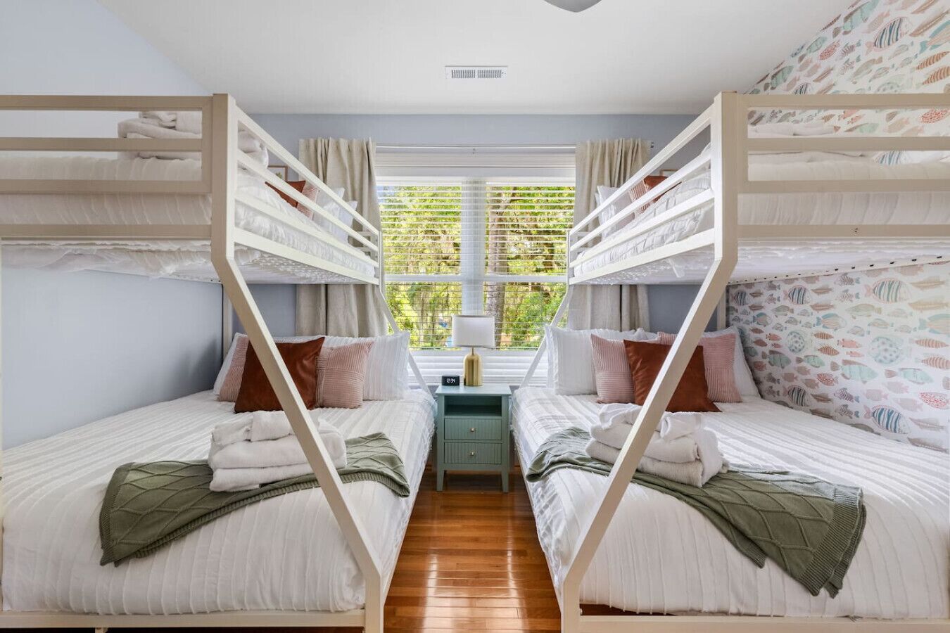 Quarto com beliches, uma escrivaninha e uma janela com cortinas.
