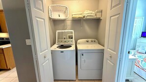 A laundry room with two washing machines, a drying rack, and a shelf with towels.