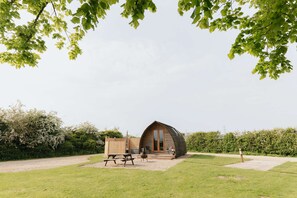 A small, wooden cabin with a pitched roof, a patio area with a table and chairs, and a view of the surrounding greenery. - Deluxe Cosy Cabin With Wood Fired Hot Tub (Spalding)