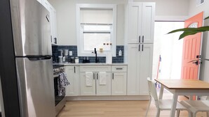 A modern kitchen with white cabinets, a stainless steel refrigerator, and a wooden dining table. - Modern 1BR in Central Philly Near Hospitals, Parks, WiFi + Housekeeping (Philadelphia)