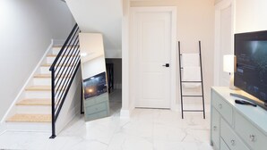 A modern interior with a staircase, a flat-screen TV, a wardrobe, and a door. - Modern 1BR in Central Philly Near Hospitals, Parks, WiFi + Housekeeping (Philadelphia)